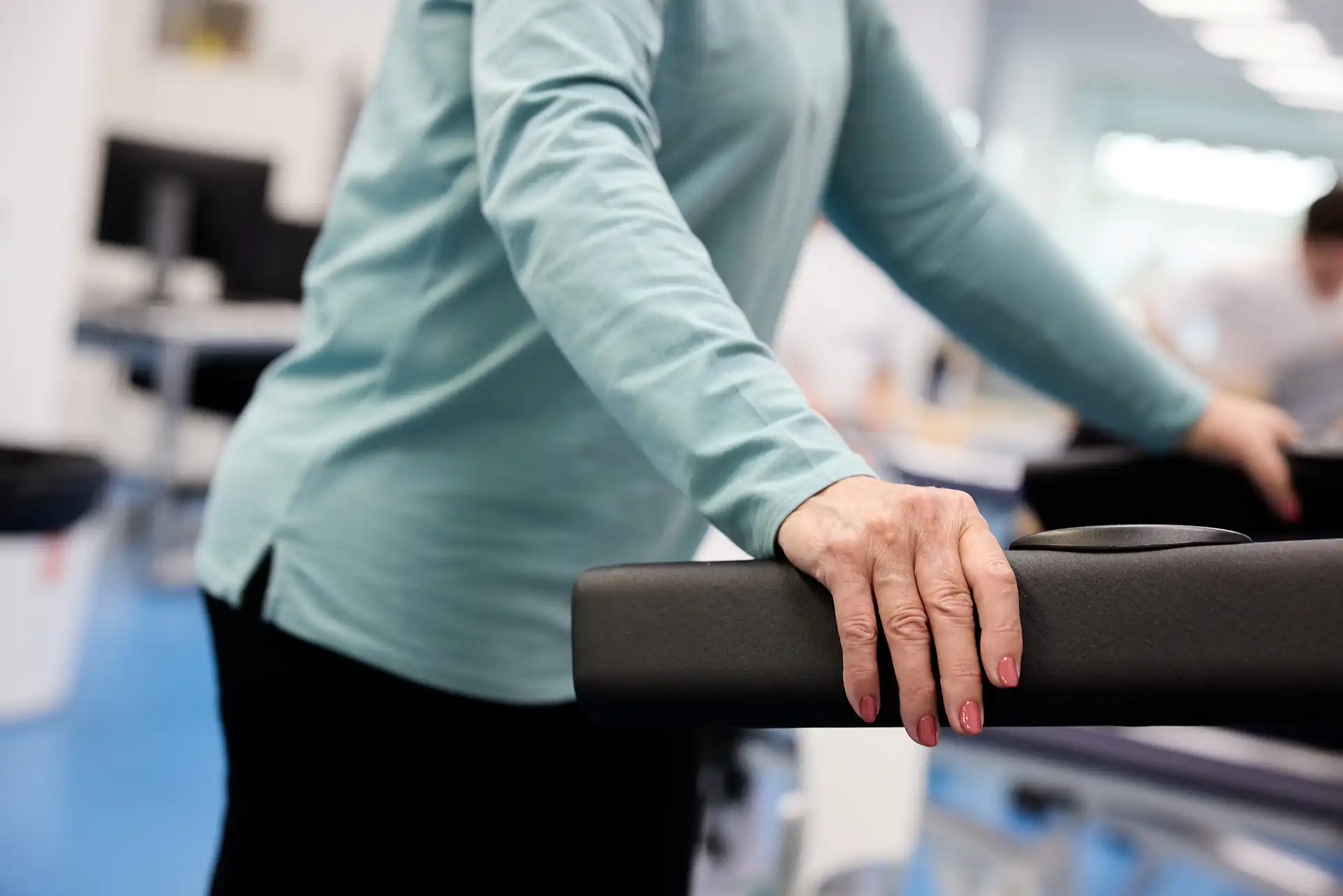 Primer pla de les mans d'una persona gran recolzades en els agafadors d'una cinta de córrer o màquina de gimnàs mentre fa exercici.